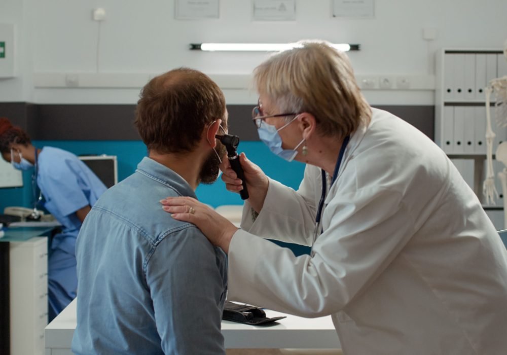 Doctor otologist examining ear infection of patient with otoscope during covid 19 pandemic. Health specialist using otology instrument to do consultation at checkup visit appointment.