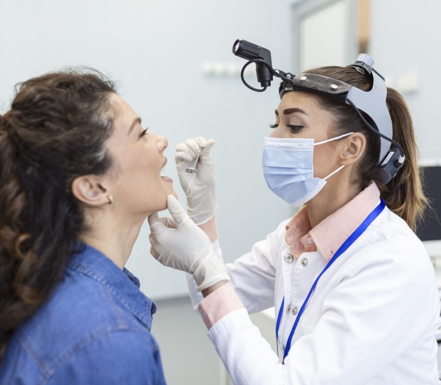Female patient opening her mouth for the doctor to look in her throat. Otolaryngologist examines sore throat of patient.